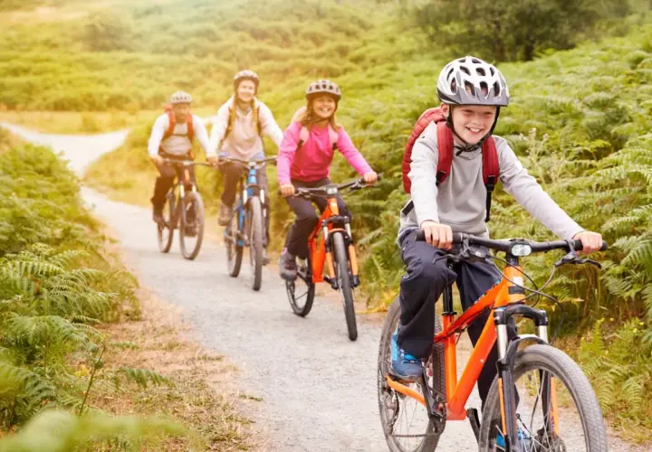 Fröhliche Familie auf einer Fahrradtour mit Kindern durch eine grüne Landschaft.
