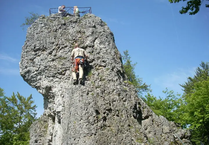Kletterer erklimmt Felsen bei der Burgruine Wolfsberg. Oben genießen zwei Personen die Aussicht.