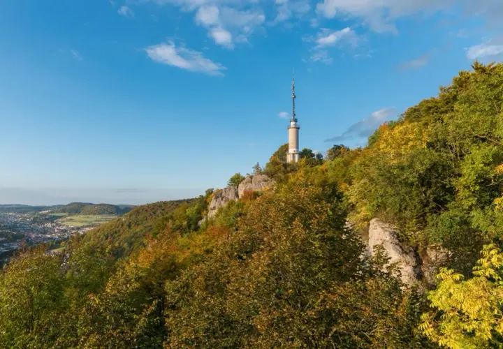 Der Schlossfelsenturm Albstadt ragt auf einem bewaldeten Felsen über der Stadt auf. Bunte Herbstfarben schmücken die Hänge.