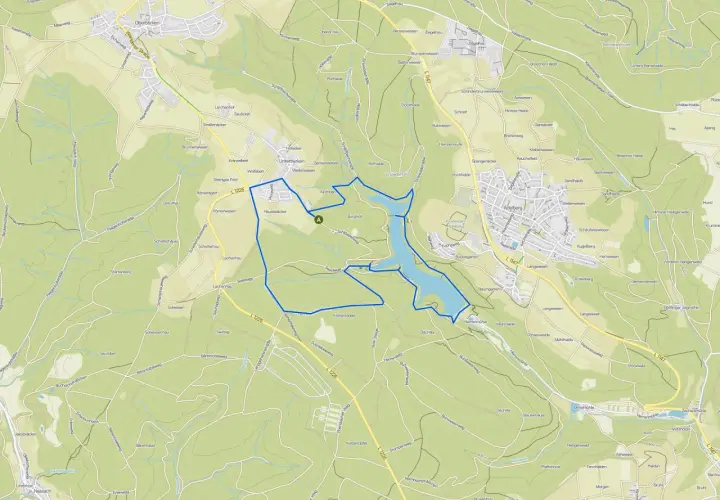 Der Herrenbachstausee mit seiner Kugelbahn-ähnlichen Uferlinie, eingebettet in grüne Hügel und Wälder.
