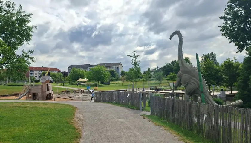 Ein riesiger Dinosaurier wacht über den Himmelsgarten mit Spielplatz.