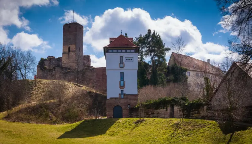 Die Ruine Wartstein mit einem modernen Turm und alten Gemäuern unter blauem Himmel mit Wolken.