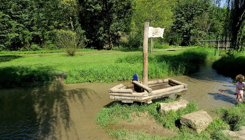 Ein hölzernes Piratenschiff mit einem Kind an Bord im Wolfstal Lauterach. Ein weiteres Kind spielt im Wasser.