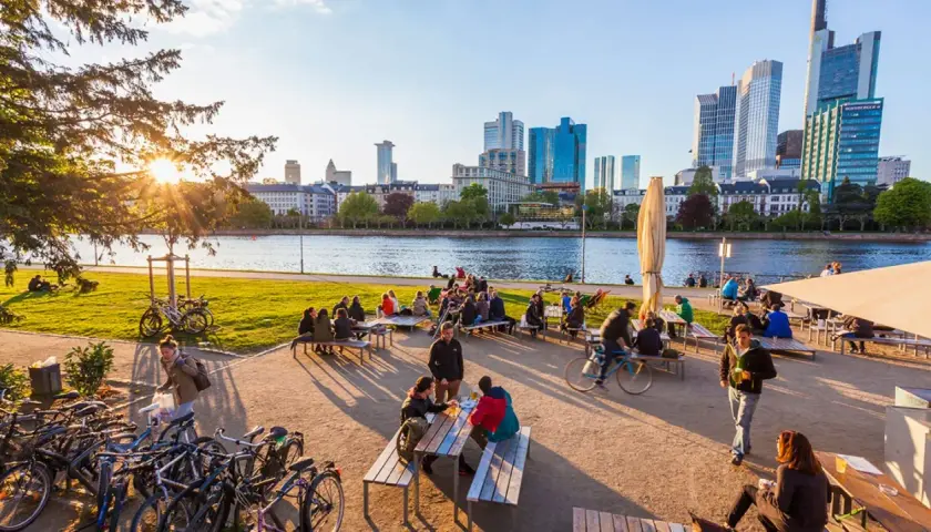 Frankfurt am Main: Menschen genießen das Leben am Mainufer mit Blick auf die Skyline. Hier kann man entspannen, Rad fahren und die Aussicht genießen.