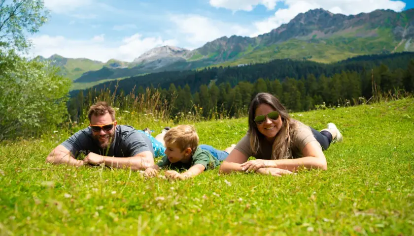 Familie genießt die Aussicht auf die Berge in der Schweiz, liegend auf einer grünen Wiese.