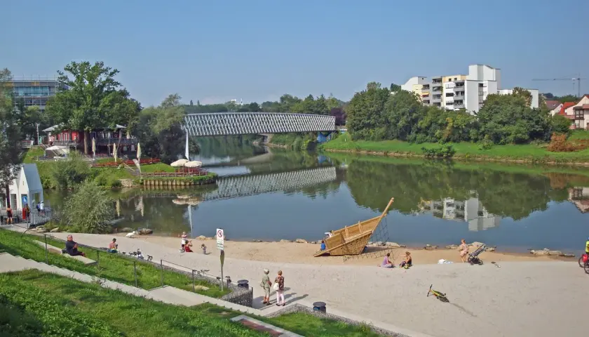 Sonniger Tag am Neckarstrand Remseck mit Menschen am Sandstrand, einem Spielschiff und einer Brücke über dem Fluss.