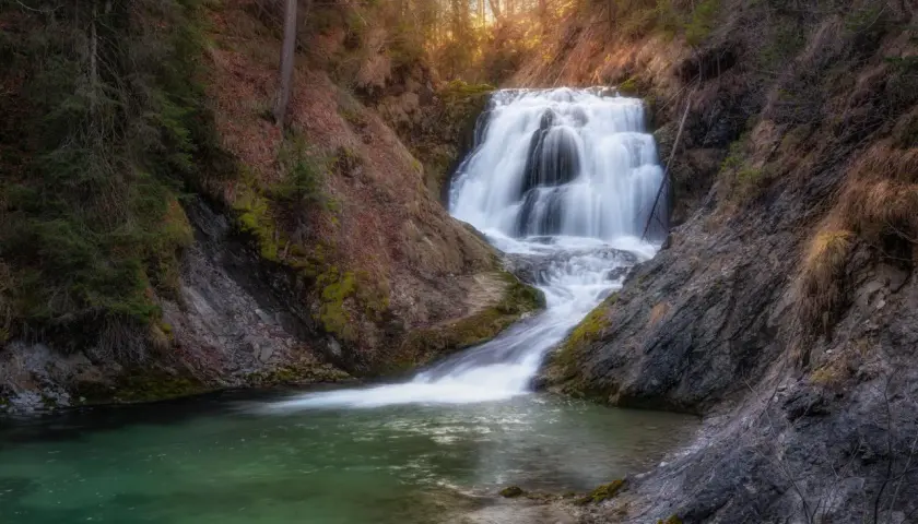 Ein malerischer Walchensee Wasserfall stürzt über Felsen in ein smaragdgrünes Becken. Umgeben von Bäumen und Moos, ein friedlicher Ort.