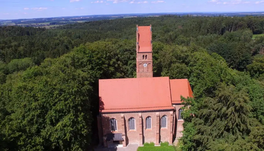 Kirche mit rotem Dach und Turm, umgeben von Wald. Ein historischer Ort, vielleicht einst Burg Wittelsbach.