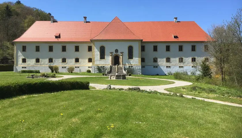 Schloss Ehrenfels bei Hayingen, ein imposantes Gebäude mit rotem Ziegeldach, umgeben von grünen Rasenflächen und Bäumen.