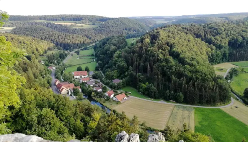 Idyllisches Lautertal Alb mit kleinen Dörfern, Flüssen und bewaldeten Hügeln, aufgenommen von einem Felsvorsprung.