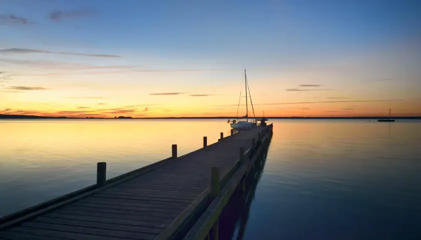 Holzsteg am Steinhuder Meer bei Sonnenuntergang, ein Segelboot liegt vertäut.