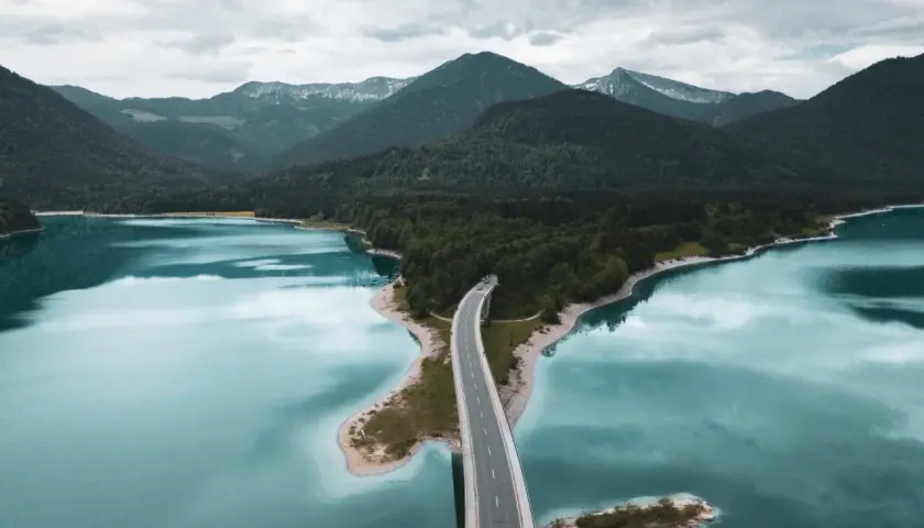 Brücke über türkisfarbenen See, umgeben von bewaldeten Bergen. Perfekt für einen Urlaub in Deutschland.