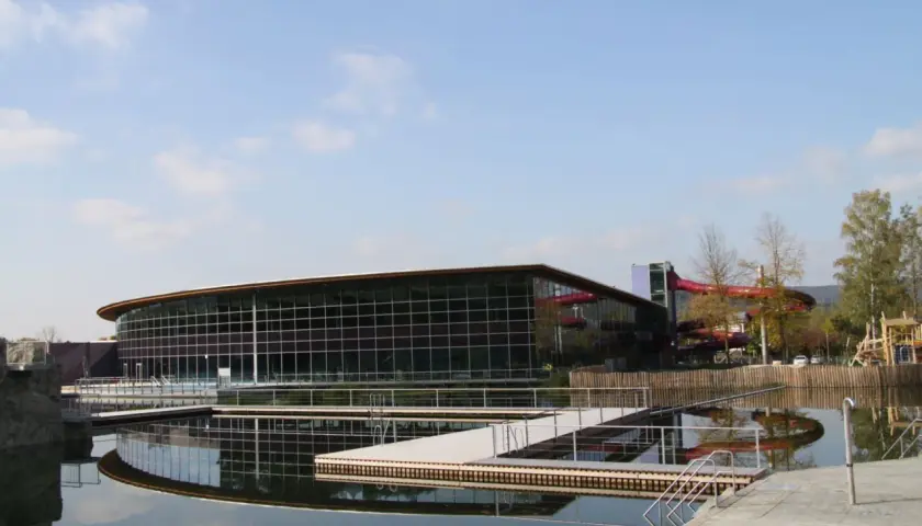 Moderner Badesee Schorndorf mit Glasfassade, Wasserrutschen und Stegen im Wasser.