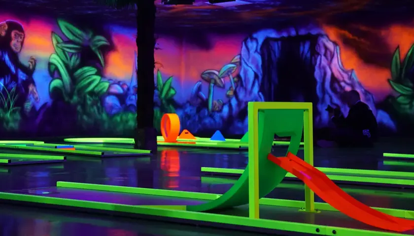 Ein Affe blickt auf leuchtende Bahnen beim Schwarzlicht Minigolf Heilbronn. Bunte Wandmalereien und Hindernisse schaffen eine Dschungel-Atmosphäre.