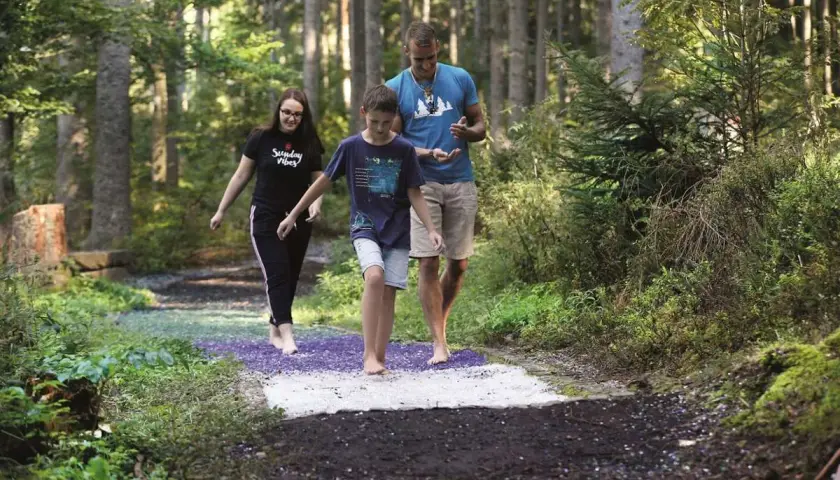 Familie genießt den Barfusspark Hallwangen. Barfuß über verschiedene Untergründe im Wald spazieren.