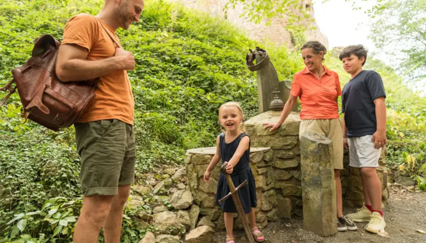 Familie erkundet die Eifel mit Kindern. Ein kleines Mädchen zieht stolz ein Schwert aus einem Stein.