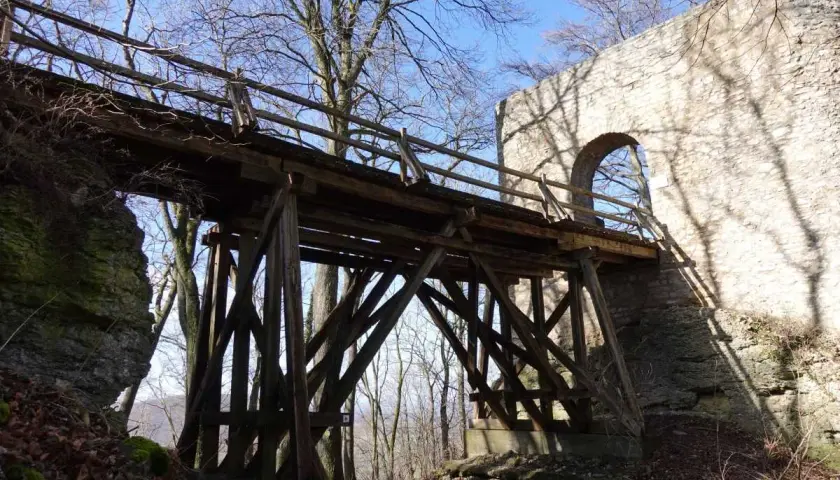 Holzbrücke führt zur Burgruine Rauber. Steinmauer mit Bogen und Schatten von Bäumen.