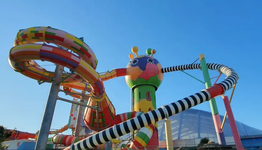 Bunte Miramar Rutschen schlängeln sich vor blauem Himmel. Ein fantasievolles Gebilde mit bunten Röhren und einem lustigen Kopf.