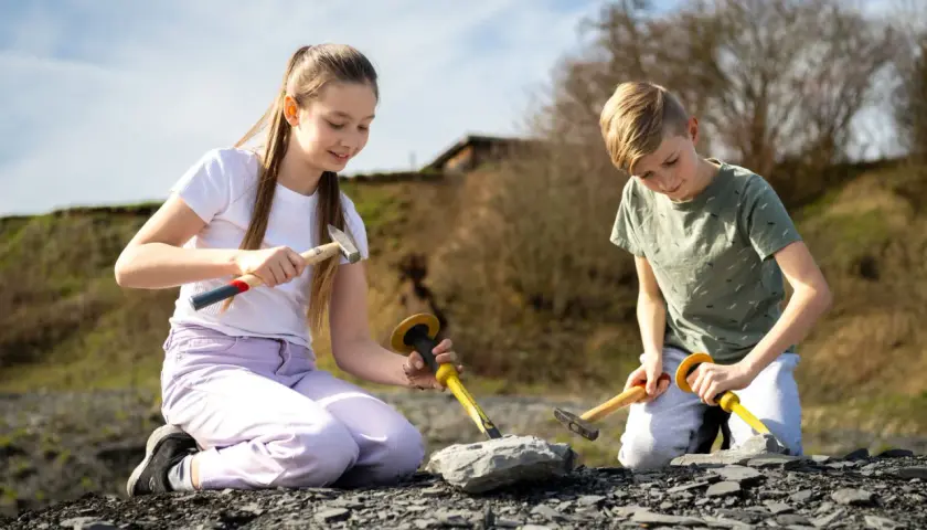 Zwei Kinder knien im Freien und graben mit Hämmern und Meißeln nach Fossilien. Vielleicht finden sie bald etwas Spannendes, wie bei Ausgrabungen in Stuttgart.