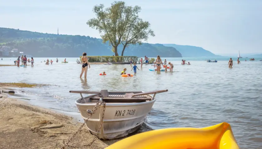 Menschen genießen das Bodensee Baden an einem sonnigen Tag. Kinder planschen im Wasser, während Boote am Ufer liegen.