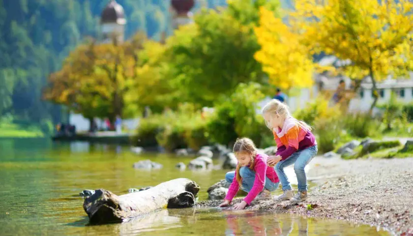 Zwei Mädchen genießen ihren Urlaub mit Kindern in Bayern am See. Sie spielen am Ufer im bunten Herbstlaub.