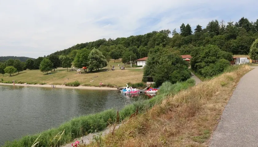 Sonniger Tag am badesee Zaberfeld. Menschen entspannen am Ufer, Kinder planschen im Wasser, Tretboote warten auf Ausflügler.