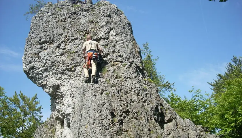 Kletterer erklimmt Felsen bei der Burgruine Wolfsberg. Oben genießen zwei Personen die Aussicht.