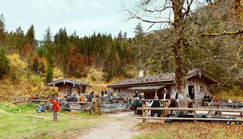 Familien genießen einen Herbsttag am Tegernsee. Kinder spielen im Gras, während Erwachsene in gemütlichen Hütten sitzen.