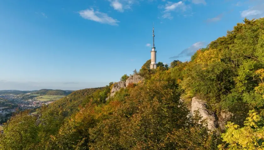 Der Schlossfelsenturm Albstadt ragt auf einem bewaldeten Felsen über der Stadt auf. Bunte Herbstfarben schmücken die Hänge.