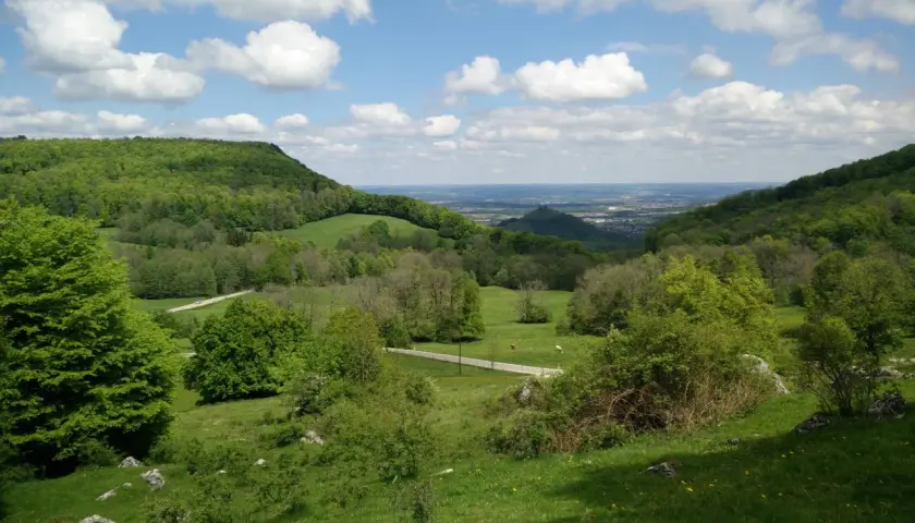 Grüne Hügel und Wiesen, ideal für eine Randecker Maar Wanderung. Wolken ziehen über das weite Tal.