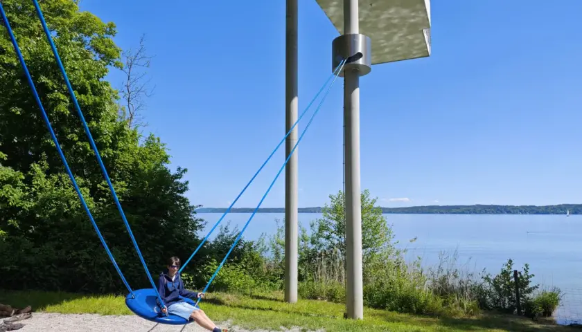 Ein Junge schaukelt am Starnberger See. Kinder genießen die Sonne und den Blick auf das Wasser.
