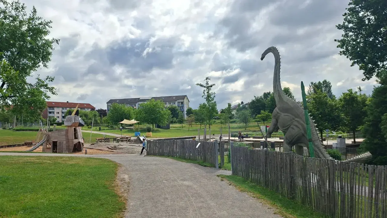 Ein riesiger Dinosaurier wacht über den Himmelsgarten mit Spielplatz.
