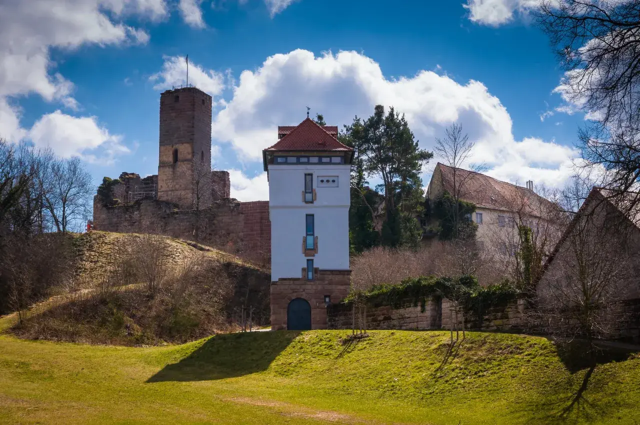Die Ruine Wartstein mit einem modernen Turm und alten Gemäuern unter blauem Himmel mit Wolken.