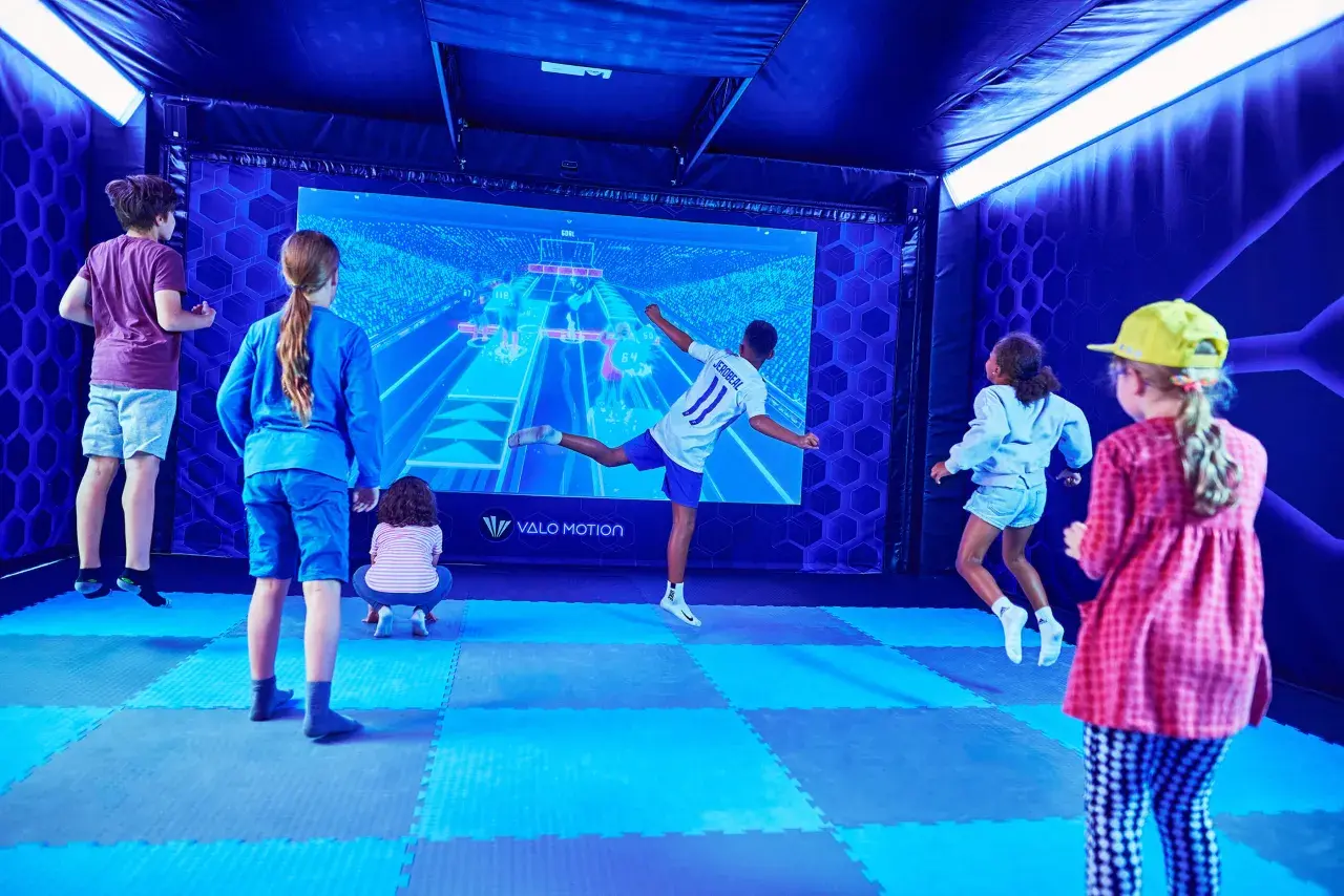 Kinder spielen in Berlin ein interaktives Spiel vor einer großen Leinwand.