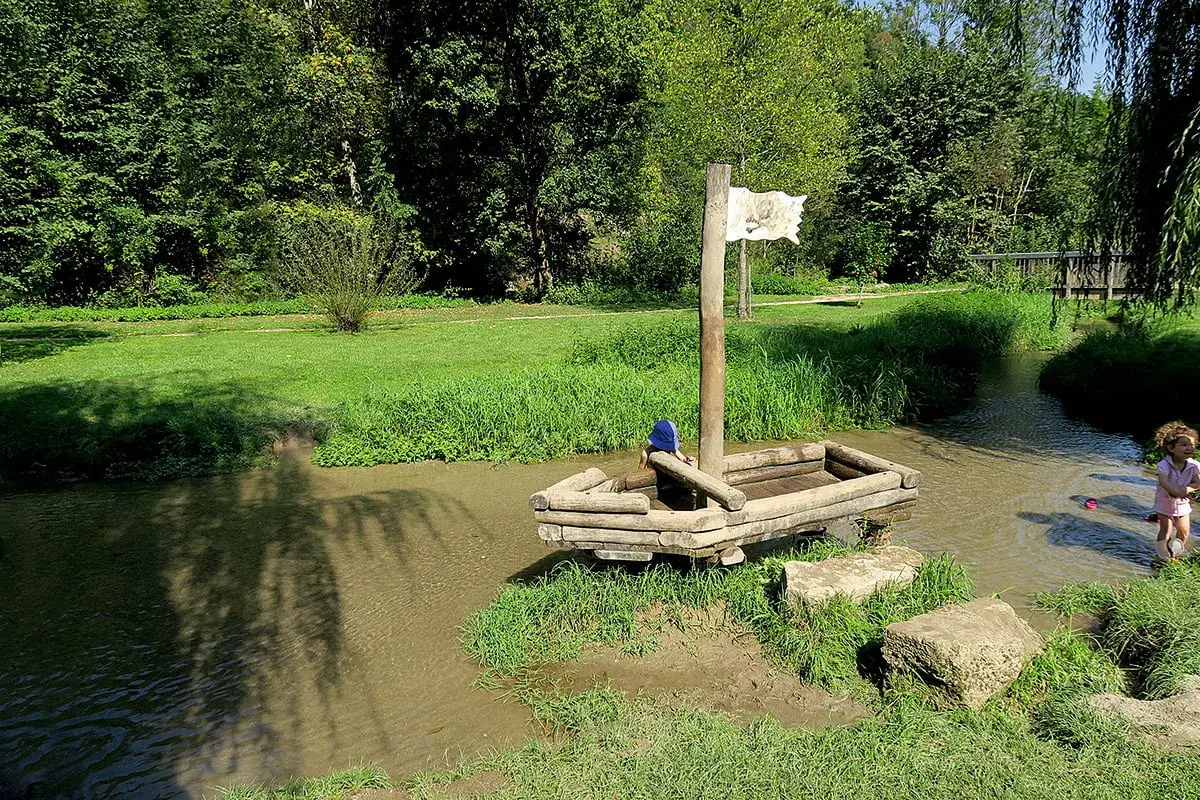 Ein hölzernes Piratenschiff mit einem Kind an Bord im Wolfstal Lauterach. Ein weiteres Kind spielt im Wasser.