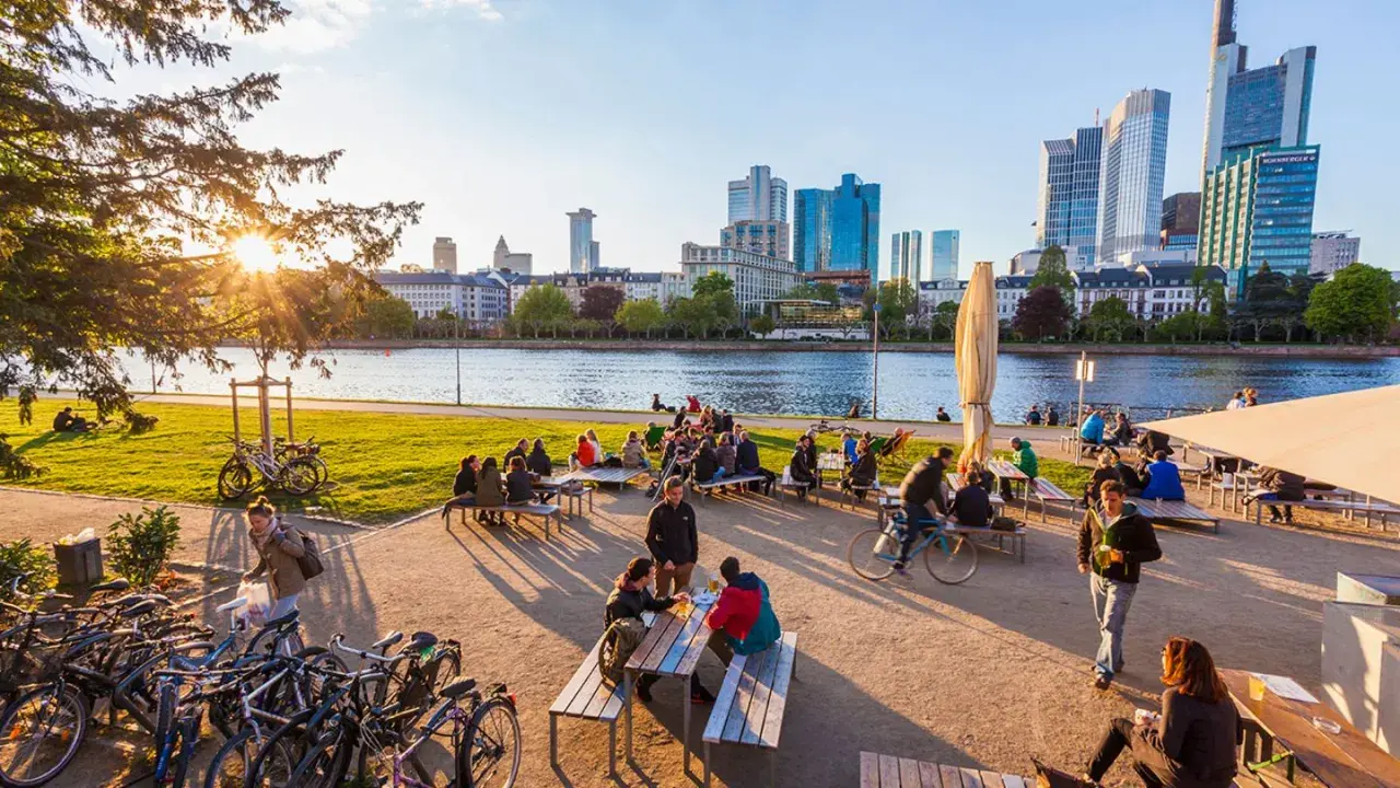 Frankfurt am Main: Menschen genießen das Leben am Mainufer mit Blick auf die Skyline. Hier kann man entspannen, Rad fahren und die Aussicht genießen.