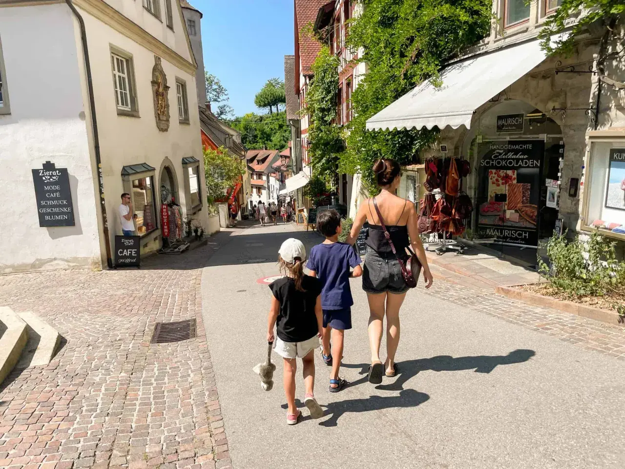 Familie spaziert durch eine Gasse am Bodensee mit Kindern, vorbei an Geschäften und Cafés.