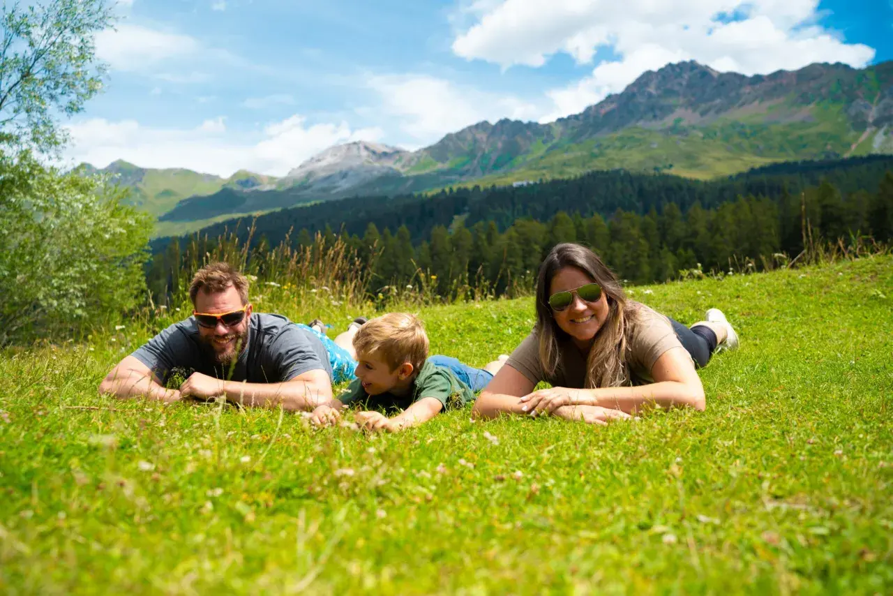 Familie genießt die Aussicht auf die Berge in der Schweiz, liegend auf einer grünen Wiese.