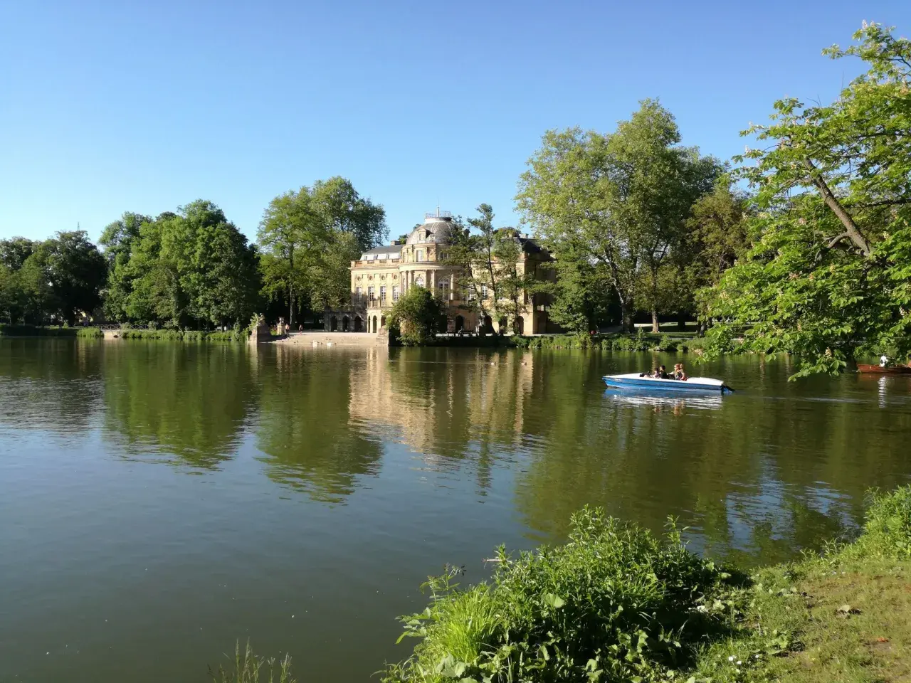 Ein Boot gleitet auf dem Monrepos-See, im Hintergrund das Schloss Monrepos. Der Monrepos-See rundweg lädt zum Spaziergang ein.