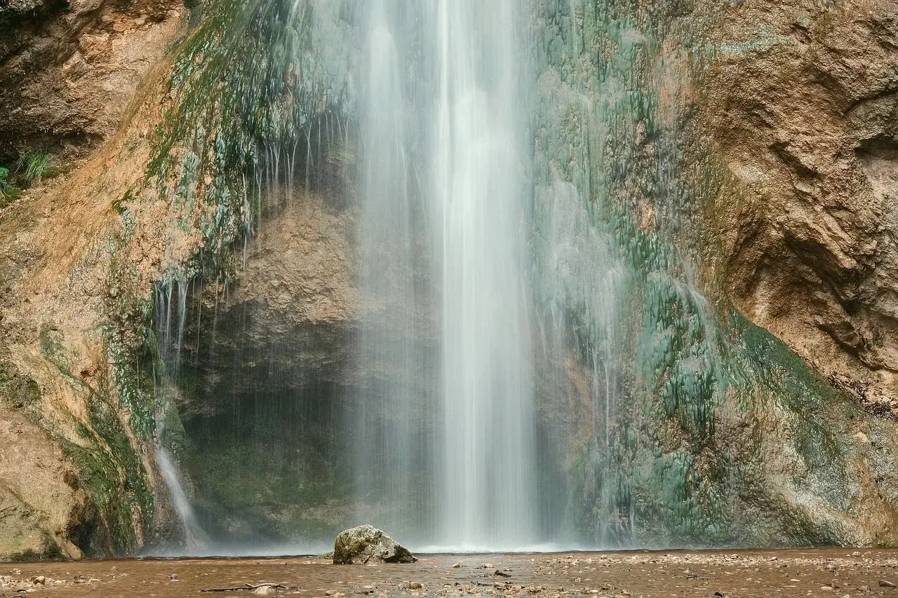 Der Drackensteiner Wasserfall stürzt über moosbewachsene Felsen. Ein einzelner Stein liegt im flachen Wasser am Fuß des Wasserfalls.