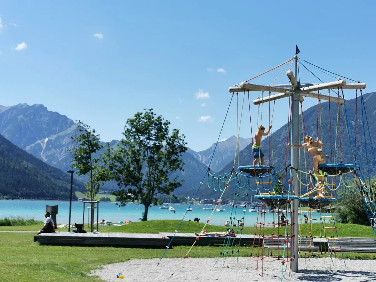Kinder klettern auf einem Spielgerüst am See. Ein toller Wasserspielplatz für Kinder mit Bergkulisse.