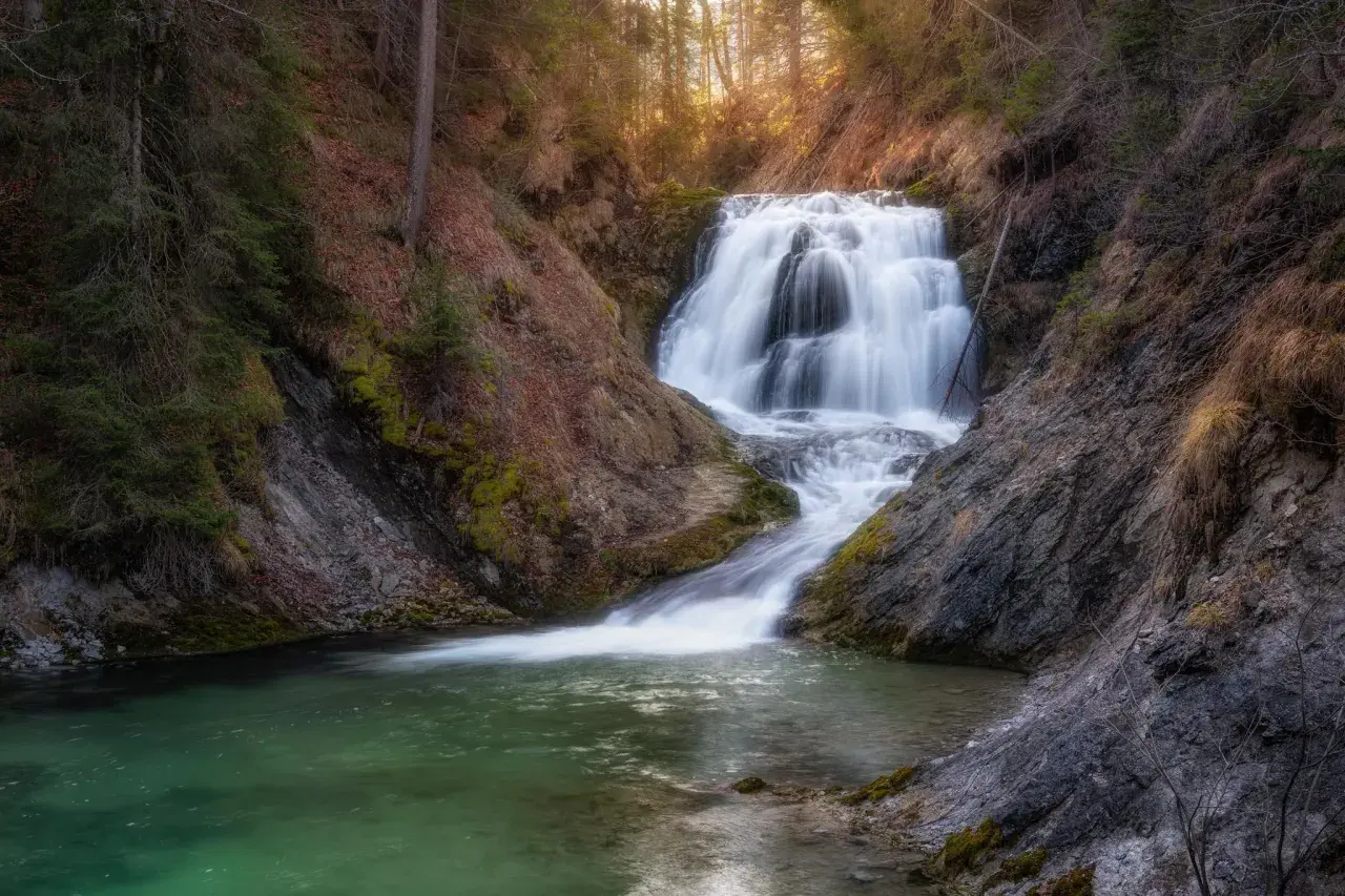 Ein malerischer Walchensee Wasserfall stürzt über Felsen in ein smaragdgrünes Becken. Umgeben von Bäumen und Moos, ein friedlicher Ort.