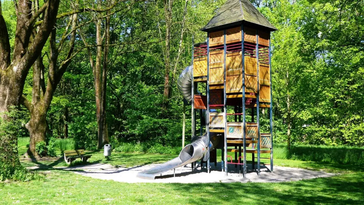 Ein hoher Holzturm mit Rutschen bildet das Zentrum eines abenteuerspielplatzes in Stuttgart. Umgeben von grünen Bäumen lädt er zum Spielen ein.