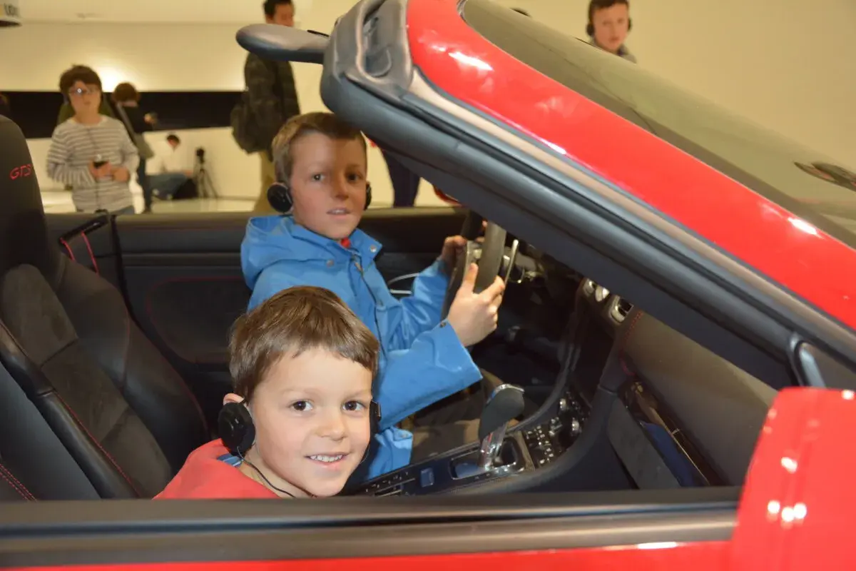 Zwei Jungen mit Kopfhörern sitzen in einem roten Porsche im Porsche Museum.
