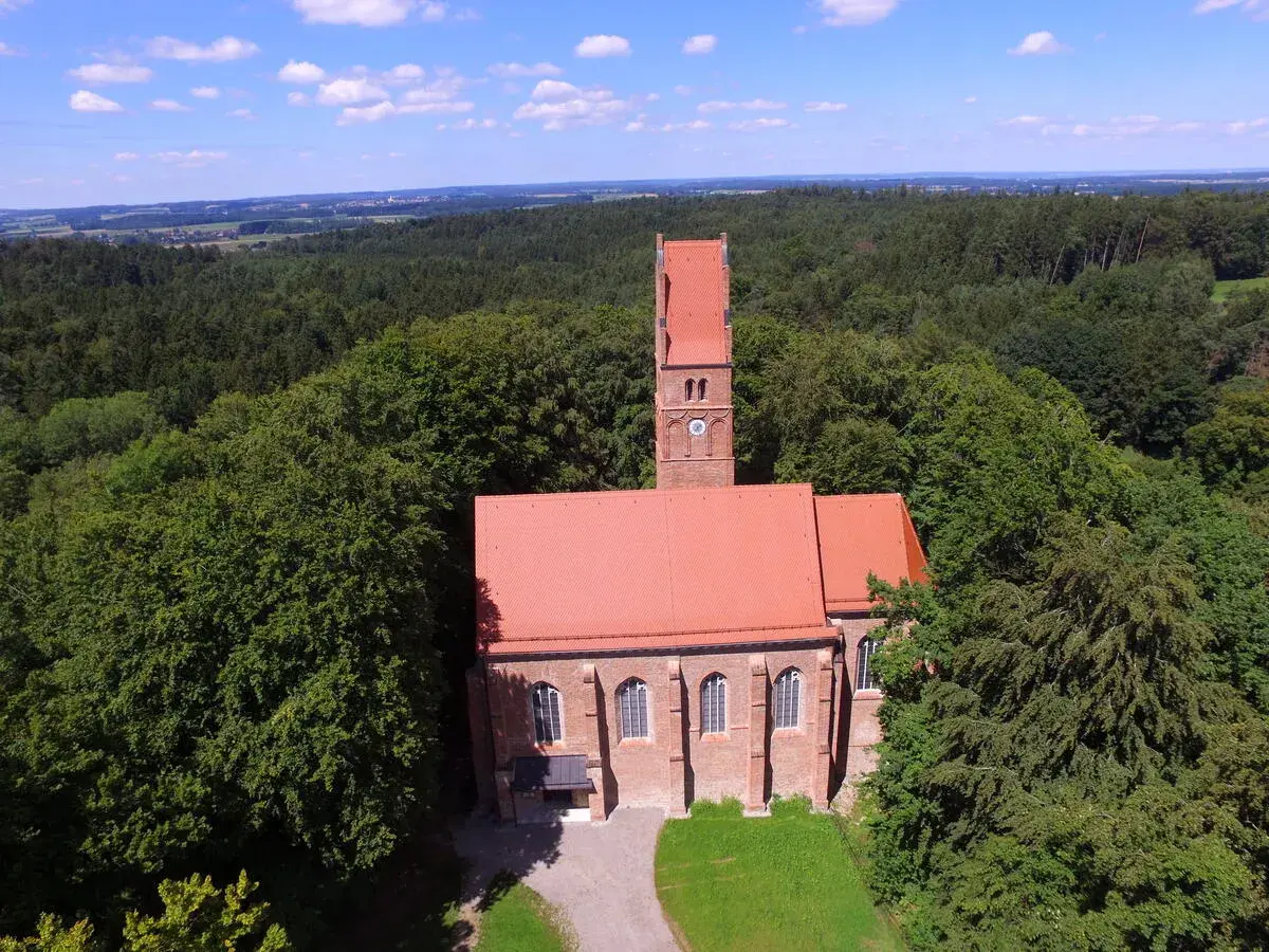 Kirche mit rotem Dach und Turm, umgeben von Wald. Ein historischer Ort, vielleicht einst Burg Wittelsbach.