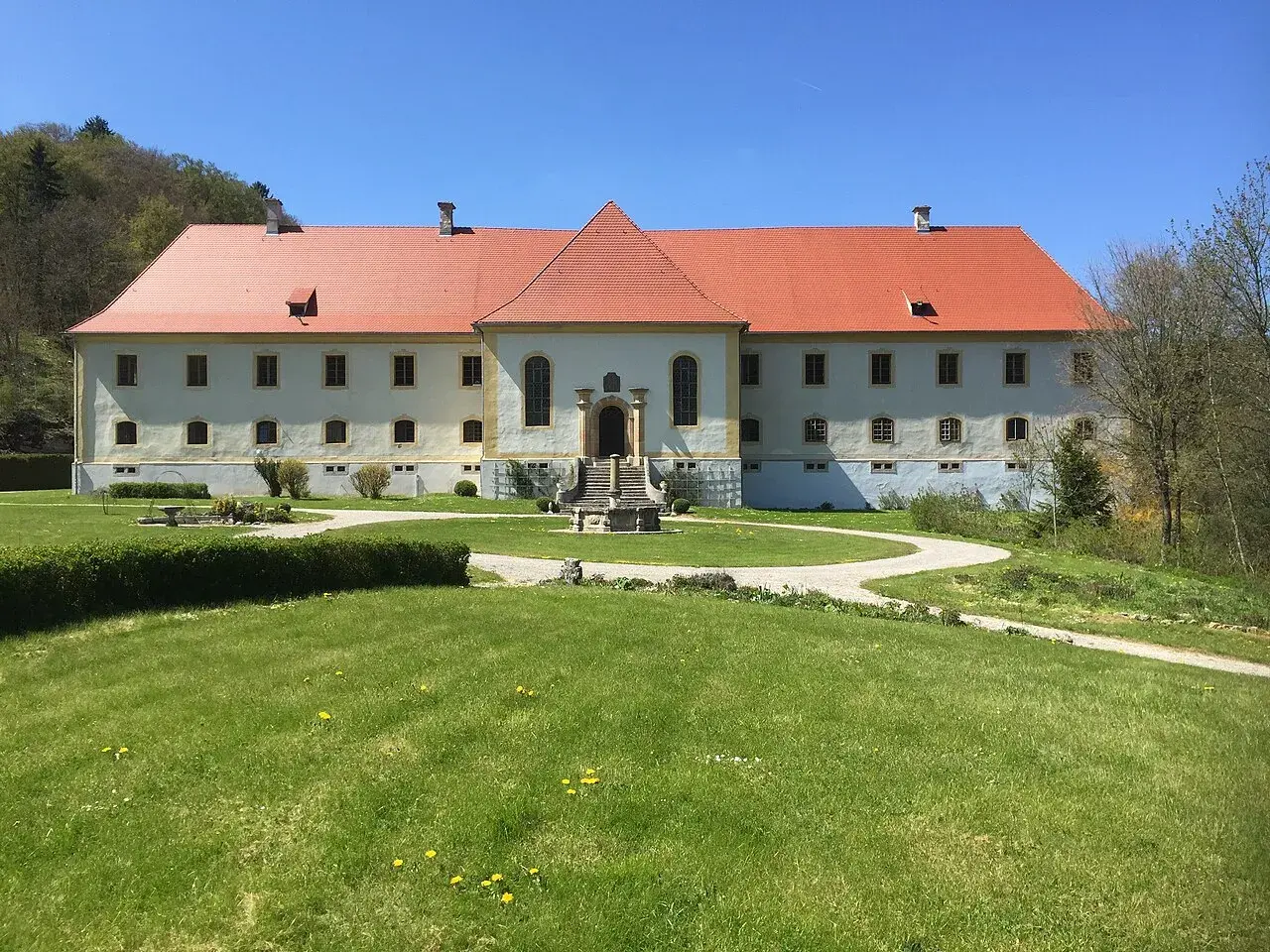 Schloss Ehrenfels bei Hayingen, ein imposantes Gebäude mit rotem Ziegeldach, umgeben von grünen Rasenflächen und Bäumen.