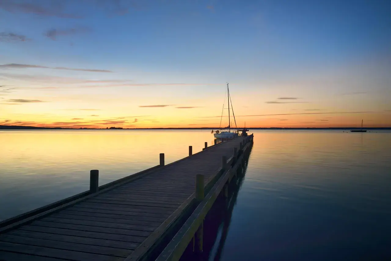 Holzsteg am Steinhuder Meer bei Sonnenuntergang, ein Segelboot liegt vertäut.