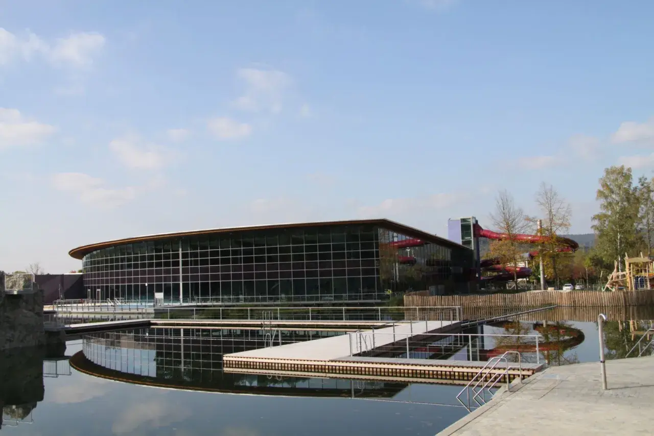 Moderner Badesee Schorndorf mit Glasfassade, Wasserrutschen und Stegen im Wasser.