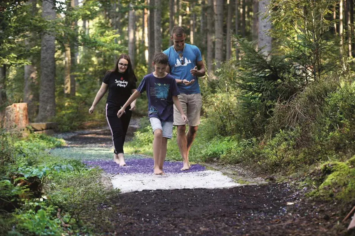 Familie genießt den Barfusspark Hallwangen. Barfuß über verschiedene Untergründe im Wald spazieren.