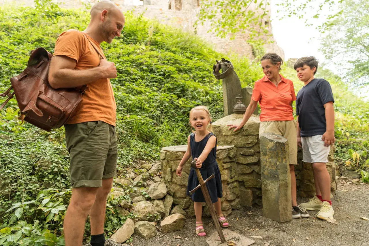 Familie erkundet die Eifel mit Kindern. Ein kleines Mädchen zieht stolz ein Schwert aus einem Stein.